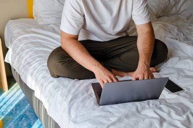 Bir adam evde ya da otellerde dizüstü bilgisayar ve akıllı telefonla çalışıyor. Uzaktan kumanda. Ofis evde. Yatak odasında bir adam dizüstü bilgisayarda yazıyor, uzaklardan öğreniyor, internette sörf yapıyor.