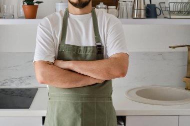 Mutfak önlüklü bir adam modern bir mutfakta duruyor. Üniformayla evde yemek pişirmek, koruyucu giysi. Yeşil kumaş önlük, günlük kıyafetler. Önlüklü bir adam yemek hazırlar.