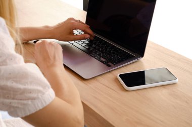 Kız dizüstü bilgisayarın önünde bir masada oturuyor ve iş için akıllı telefon kullanıyor. Evden uzak bir iş. Bilgisayarı ve akıllı telefonu olan bir ofis masası. İş geçmişi. Merkez Ofis