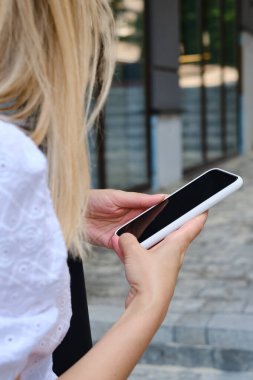 Woman is holding a modern smartphone, sending a text message or using an app on her mobile phone. Internet technology user. Smartphone close-up. Focus on the phone screen
