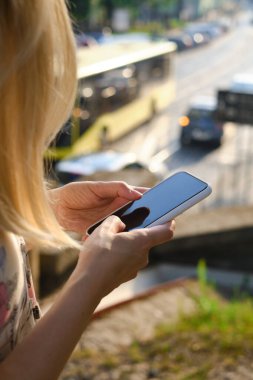 Sokaktaki bir kız elinde modern bir akıllı telefon tutuyor, mesaj gönderiyor ya da cep telefonunda bir uygulama kullanıyor. Şehir haritasını akıllı telefondan göster. Akıllı telefon, yakın plan.