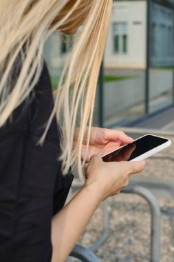 Sokaktaki bir kız elinde modern bir akıllı telefon tutuyor, mesaj gönderiyor ya da cep telefonunda bir uygulama kullanıyor. Şehir haritasını akıllı telefondan göster. Akıllı telefon, yakın plan.