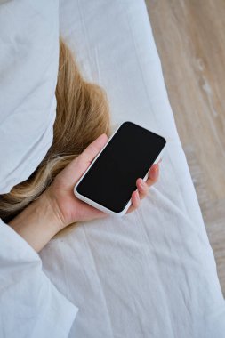 Yatakta akıllı telefonu tutan bir elin yakın çekimi. Kız alarmı kapatmak ya da bir mesaj okumak için cep telefonuna uzandı. Adam elinde bir telefonla uyuyakaldı.