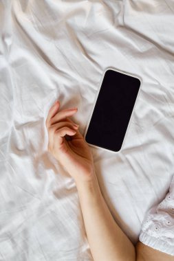 Yatakta akıllı telefonu tutan bir elin yakın çekimi. Kız alarmı kapatmak ya da bir mesaj okumak için cep telefonuna uzandı. Adam elinde bir telefonla uyuyakaldı.