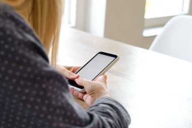 Bir kız elinde modern bir akıllı telefon tutuyor, mesaj gönderiyor ya da cep telefonunda bir uygulama kullanıyor. Gadget bağımlılığı. Akıllı telefon, yakın plan. Telefon ekranına odaklan.