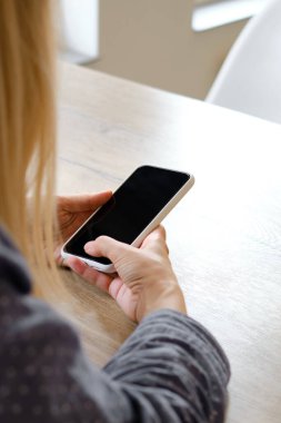 Bir kız elinde modern bir akıllı telefon tutuyor, mesaj gönderiyor ya da cep telefonunda bir uygulama kullanıyor. Gadget bağımlılığı. Akıllı telefon, yakın plan. Telefon ekranına odaklan.