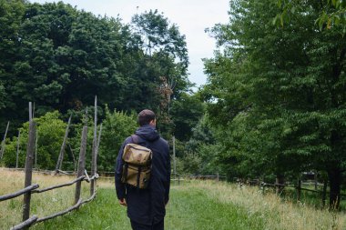 Sırt çantalı bir adam kırsalda yürüyor ve güzel etnik mimarinin tadını çıkarıyor. Açık hava macerası. Ülkede dinlenmek. Seyahat ve keşif. Sağlıklı yaşam tarzı