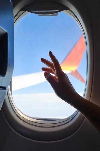 Woman looks out the window of an airplane. Hand near the porthole. Girl on the plane. Airplane wing, scenic view. Beautiful cloud, blue sky. Traveling by plane, adventure. Air transport. Aviation