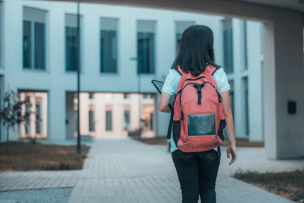 小女孩背着背包穿过大学校园走进教室 图库图片