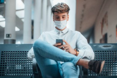 Tren istasyonunda maskeli genç bir çocuk telefonla konuşuyor.