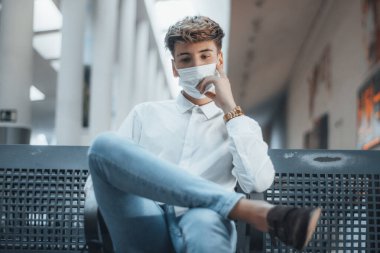 Otobüs durağındaki maskeli sarışın çocuk endişeleniyor.