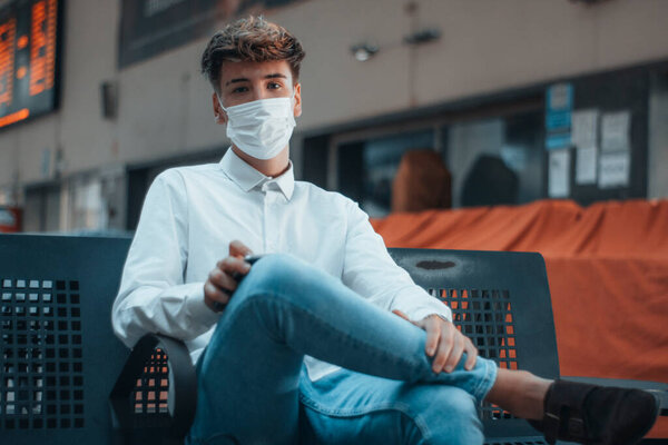 Young blond man with sad face mask at train station.