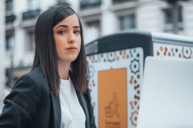 Öfkeli ve melankolik bir iş kadını. Kasaba meydanında işini yapıyor. Bilgisayarıyla birlikte son eserlerini yazıyor.