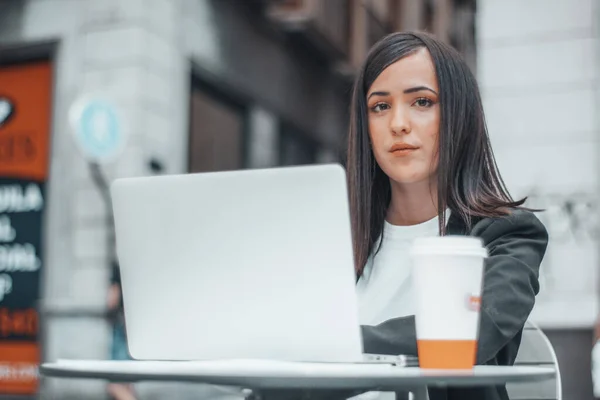年轻的棕色头发的女商人在市区食堂喝咖啡，她的笔记本电脑旁边挂着笑容，准备为公司工作 — 图库照片