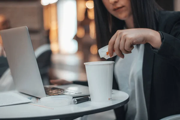 在城市广场的一家自助餐厅里，年轻的经理一边用笔记本电脑，一边往咖啡店里倒糖 — 图库照片