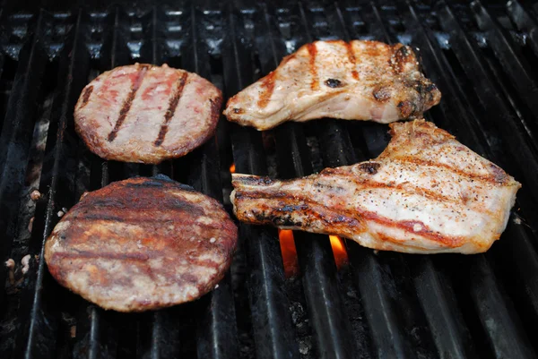Chuletas de cerdo y hamburguesas cocinando a la parrilla — Foto de Stock