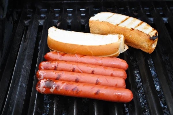 Perros calientes y panecillos cocinando en una parrilla caliente — Foto de Stock