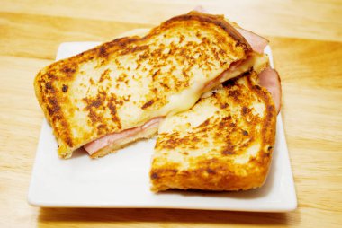 Izgara peynir ve jambonlu sandviç. Beyaz tabakta servis ediliyor.