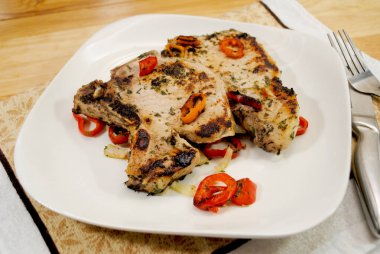 Beyaz bir tabakta soğanlı domuz pirzolası ve Mini tatlı biberli.