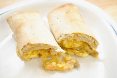 Beyaz tabakta servis edilen kahvaltılık burrito 'nun yakın çekimi.