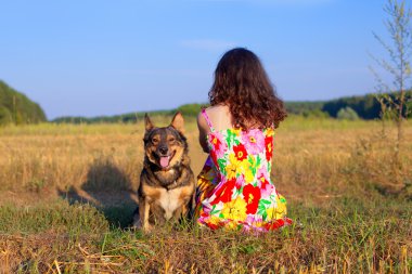 молода жінка, що сидить зі своєю собакою на лузі на заході сонця