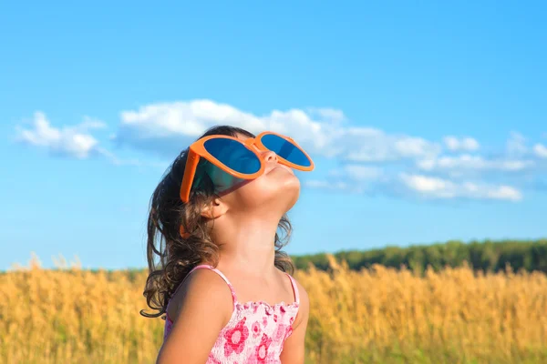 Щаслива маленька дівчинка з великими сонцезахисними окулярами дивиться на небо — стокове фото