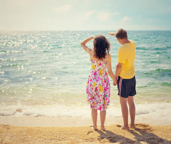 Giovane coppia che si tiene per mano rimanendo sulla spiaggia di nuovo alla fotocamera e guardando sul mare — Foto Stock