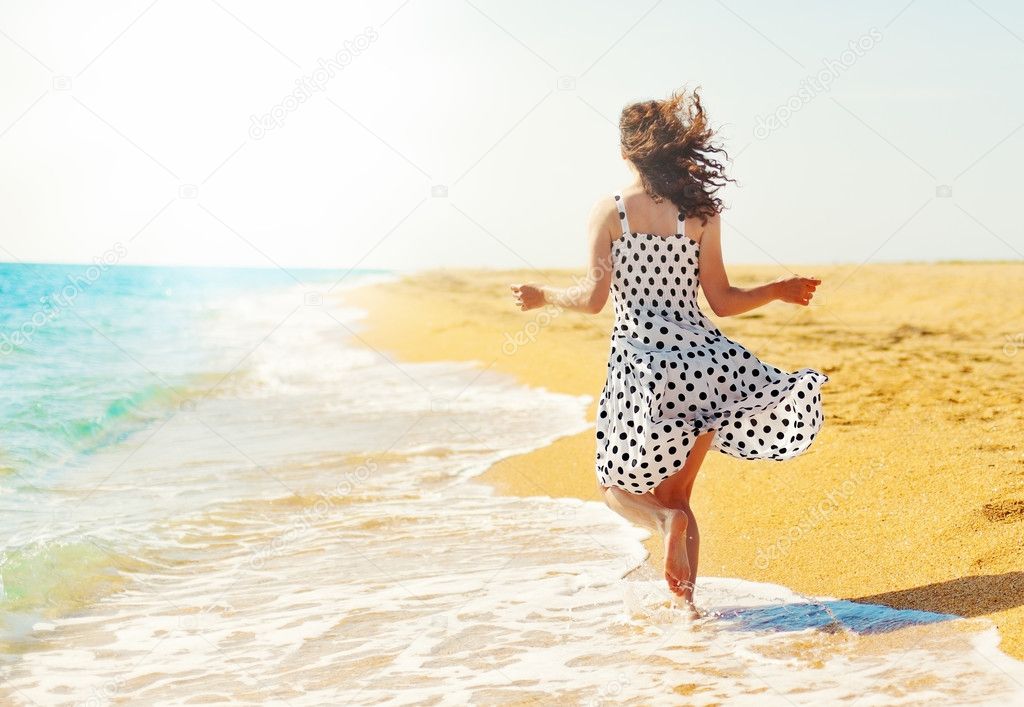 Young happy woman running on the beach back to camera