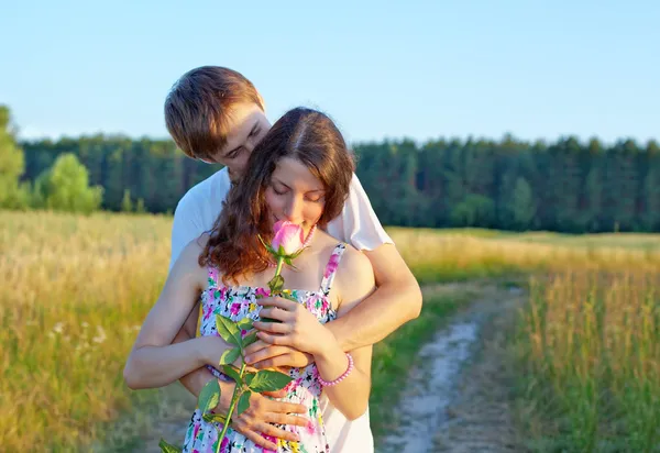 Milující mladý muž objímala svou přítelkyni s růží v ruce — Stock fotografie