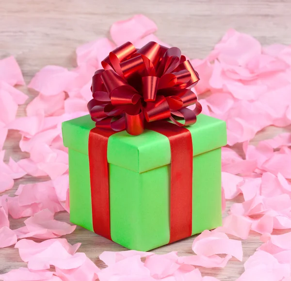 Green gift with a red ribbon on the rose petals — Stock Photo, Image