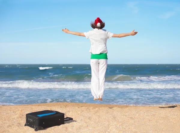 Young happy girl wearing Santa's hat jumping on the beach — Stock Photo, Image