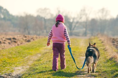 Küçük kız köpekle yürüyor.