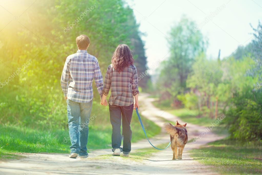 Young couple holding hands and walking with their dog in the village