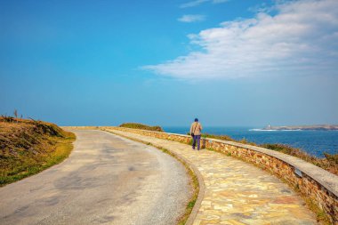 Bir adam güneşli bir günde deniz kenarında gezinti güvertesi yolu boyunca yürür (Estrada do faro)