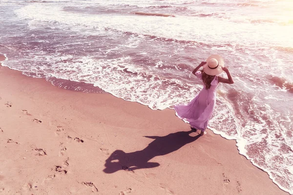 夏天阳光灿烂的季节里的海景 夏天海滩上的女人一个年轻而快乐的女人 手插在空中 穿着粉色飘逸的裙子 戴着草帽 无忧无虑地走在海边 从上面看 — 图库照片