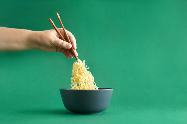 Female hand holding chopsticks with noodle in the dark grey bowl on green