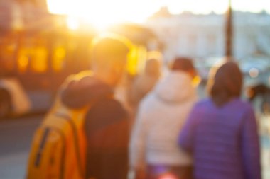 Bulanık bir arkaplan ve altın saatinde şehirde yürüyen insanlar.