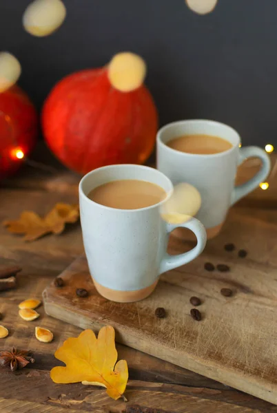 Two flavored pumpkin coffee with spices in ceramic cups on a wooden table with orange pumpkins in the background. Bokeh. Autumn mood. Time to drink hot beverage.