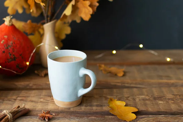 One ceramic cups with pumpkin coffee with spices on a wooden table with dry oak leaves in a vase. Autumn mood. Time to drink hot beverage. Copy space.