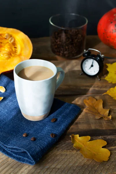 Flavored pumpkin coffee with spices in a ceramic cup on a blue napkin with orange pumpkins and dry leaves in the background. Autumn mood. Time to drink hot beverage.