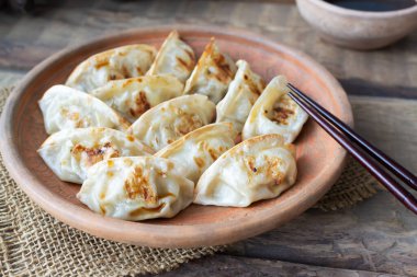 Susam tohumlu Gyoza ve soya soslu seramik bir tabakta mikro yeşiller ve ahşap bir masada bambu çubukları. Kırsal tarzda. Geleneksel Asya yemekleri konsepti. Horisontal oryantasyon. Yakın plan..