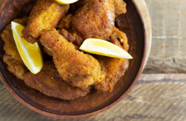 Tahta arka planda seramik tabakta limon dilimli tavuk kanatları ve bacakları. Abur cubur konsepti. Üst görünüm.