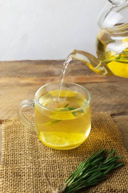 Sıcak sıcak çay bir bardak biberiye, limon ve bala karıştırılır. Tahta bir masanın üzerindeki cam çaydanlıktan. Kırsal tarzda. Alternatif tıp konsepti. Dikey oryantasyon. Seçici odak.