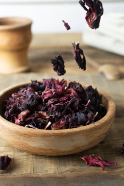 Kuru amber yaprakları ahşap bir masanın üzerindeki ahşap bir kaseye düşer, çay hazırlığı için. Kırsal tarzda. Kurutulmuş rosella ya da Sudan gülü çiçeği. Arap ülkelerinde çok popülerdir. Kestane rengi var..