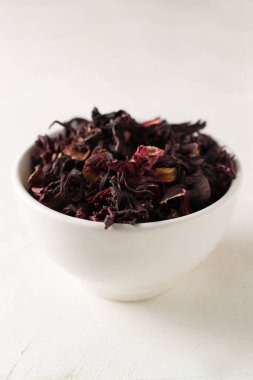 Beyaz arka planda beyaz bir kasede duran kuru amber yaprağı. Kurutulmuş rosella ya da Sudan gülü çiçeği. Arap ülkelerinde çok popülerdir. Kestane rengi var. Dikey yönelim.