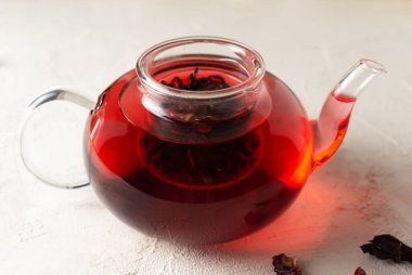Beyaz arka planda mayalanmış ambar yapraklı cam çaydanlık. Kırmızı çay. Geleneksel içki konsepti. Rosella veya Sudan gülü çiçekleri Arap ülkelerinde çok popüler bir içecektir..