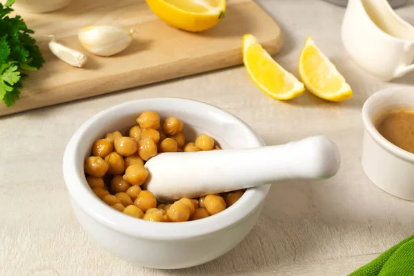 Add boiled chickpeas to Garlic with lemon juice in a ceramic mortar. Ingredients for making hummus. Boiled chickpeas, tahini, garlic, lemon and butter. A traditional Middle Eastern dish. Step by step.
