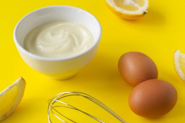 Beyaz bir kasede yumurta ve limon dilimleri ve sarı arka planda çırpılmış çırpılmış ev yapımı mayonez. Düzgün beslenme kavramı. Yaratıcı. Yatay yönelim.