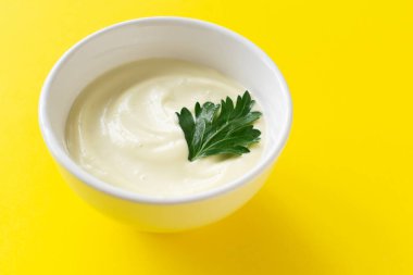 Beyaz kâse içinde ev yapımı mayonez ve sarı arka planda yeşil maydanoz yaprağı. Düzgün beslenme kavramı. Yaratıcı. Minimalizm. Yatay oryantasyon. Boşluğu kopyala.