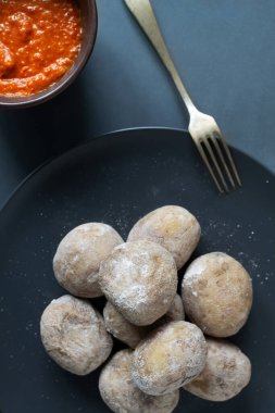 Kırmızı soslu siyah tabakta patates. Geleneksel bir Kanarya yemeği papas arrugadas 'dır. Sebzeler bol tuzlu suda kaynatılır. Üst Manzara. Boşluğu kopyala.